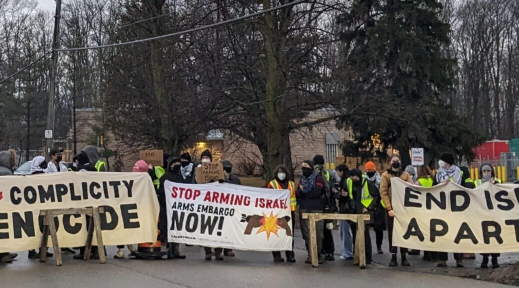 Many demonstrators stand outside the arms manufacturer Colt Canada holding signs that read 'End Complicity in Genocide', 'Stop Arming Israel, Arms Embargo Now', and 'End Israeli Apartheid'.