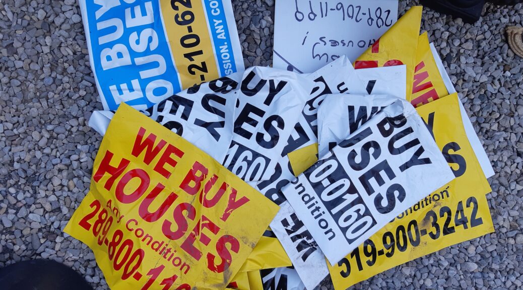 A pile of stickers and signs with "We Buy Houses" and different phone numbers.