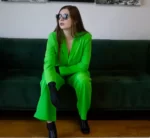 (Alyssa DVM wearing a bright green pantsuit sitting on a black leather couch)