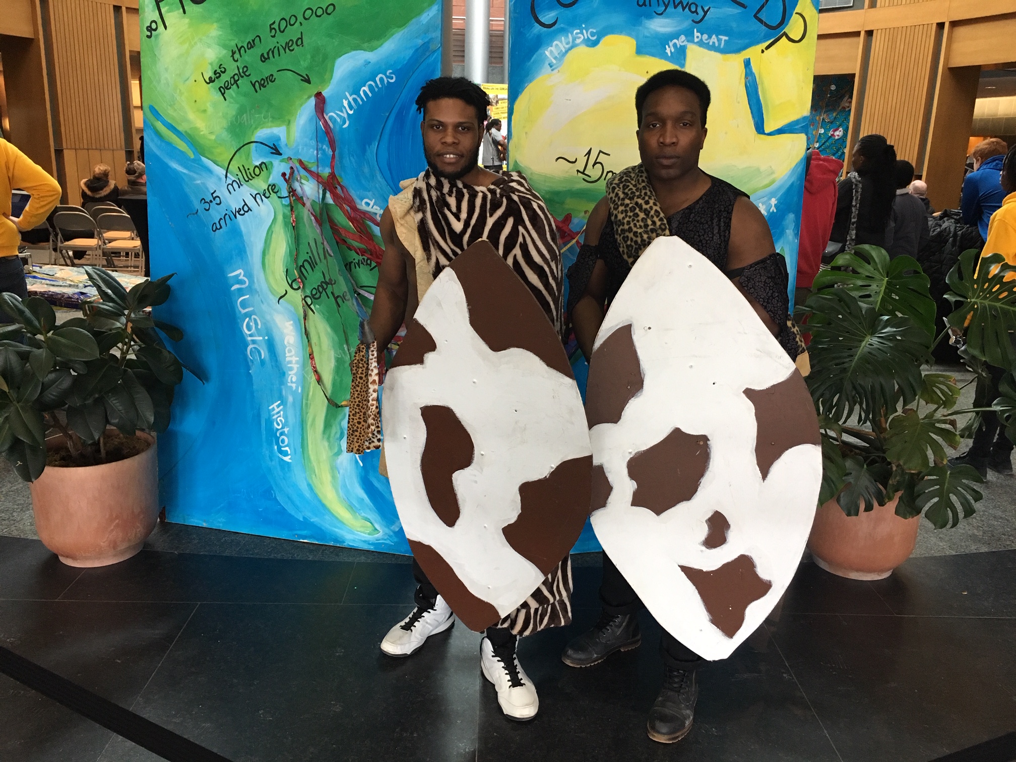 Two people carrying African shields in front of a map