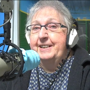 Barbara Spronk (a woman with grey hair wearing headphones and speaking into a microphone)