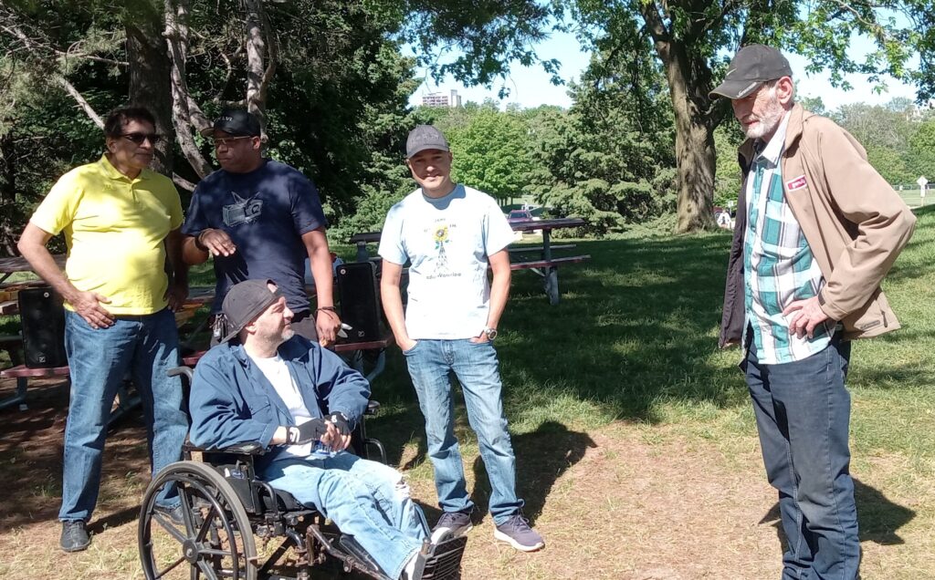 People talking to each other under a tree, some in shade, one person in a wheelchair