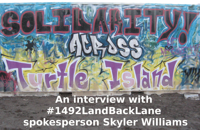 A storage container at the 1492 LandBackLane site. with the words "An interview with 1492LandBackLane spokesperson Skyler Williams" superimposed on the bottom of the picture in bold white text. The side of the container has been stylishly and colourfully painted with the words "Solidarity Across Turtle Island".
