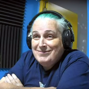 Cait Glasson sporting green hair and wearing headphones smiles towards the camera