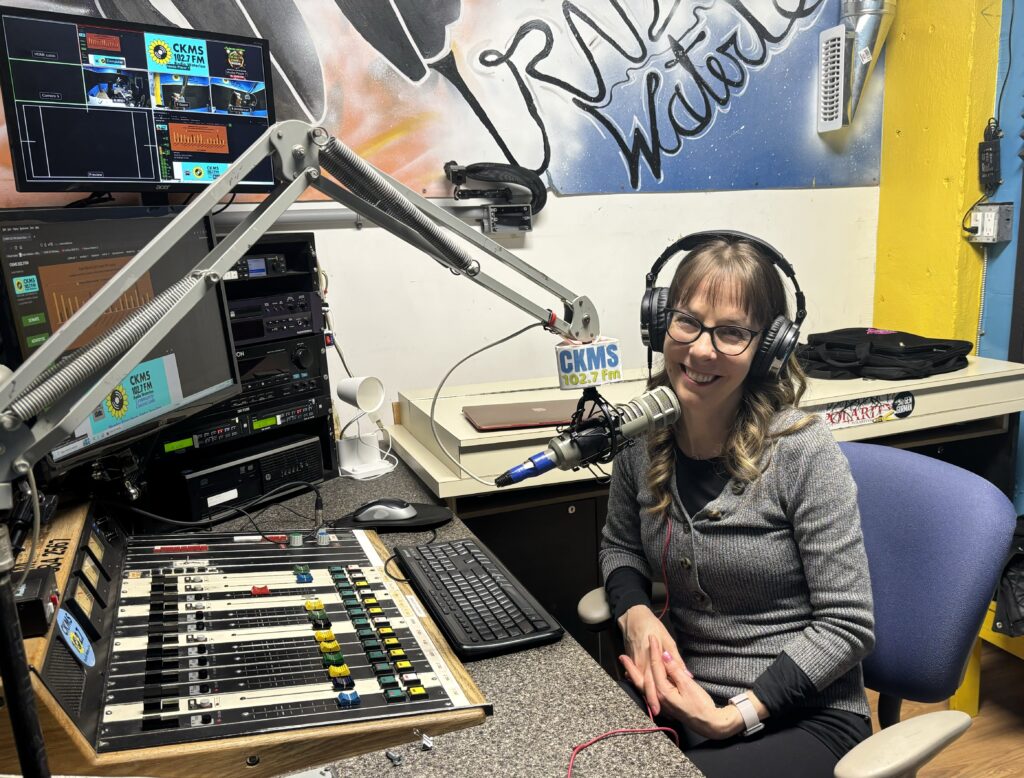 Jody Swannell sitting in the studio with sound board, audio console and microphone