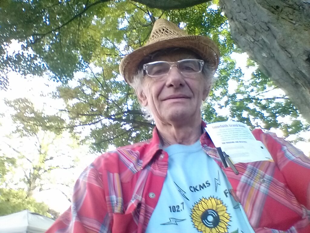 Selfie of Jeff Stager, an man wearing a straw hat, glasses, and a red plaid shirt over a CKMS-FM T-shirt