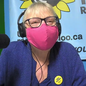 Margaret Jackson wearing a bright pink N95 mask and headphones, with a "Write For Rights" button on her blue sweater.