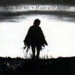 Neil Young - Harvest Moon (silhouette of a man wearing a coat with fringes, walking in a meadow under a cloudy sky)