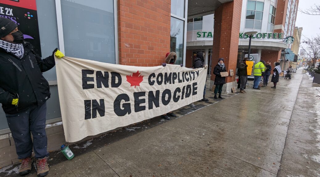 Pro-Palestinian protestors outside the Scotiabank in Uptown Waterloo display placards and a banner that reads 'End complicity in Genocide'