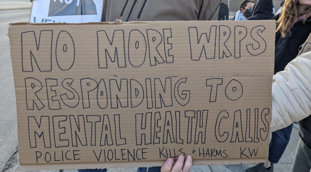A cardboard sign held by demonstrators reads 'No more WRPS responding to Mental Health Calls. Police Violence Kills and Harms KW' at the demonstration on February 23 against the fatal police shooting of Nicholas Nembhard, a 31-year-old black man who was in the midst of a mental health crisis