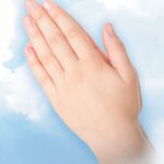 (praying hands on a background of wispy clouds on light blue)