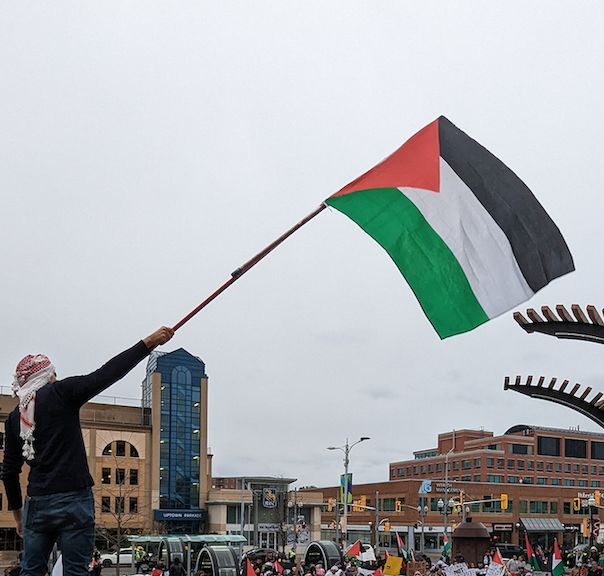 A man wearing the kaffiyeh waves a large Palestinian flag over the crowd gathered in Uptown Waterloo to show support for the Palestine territories