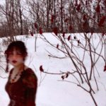 (A woman in a red dress walking through deep snow, a bare branch with only a few leaves is in the foreground)