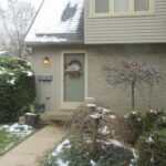 (photo of a the front door of a detached house, with snow-covered shrubbery in front)