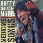 Buffy Sainte-Marie | Medicine Songs (Bubby Sainte-Marie with eyes closed, holding a mic in her right hand, and with her left arm outstretched towards the viewer)