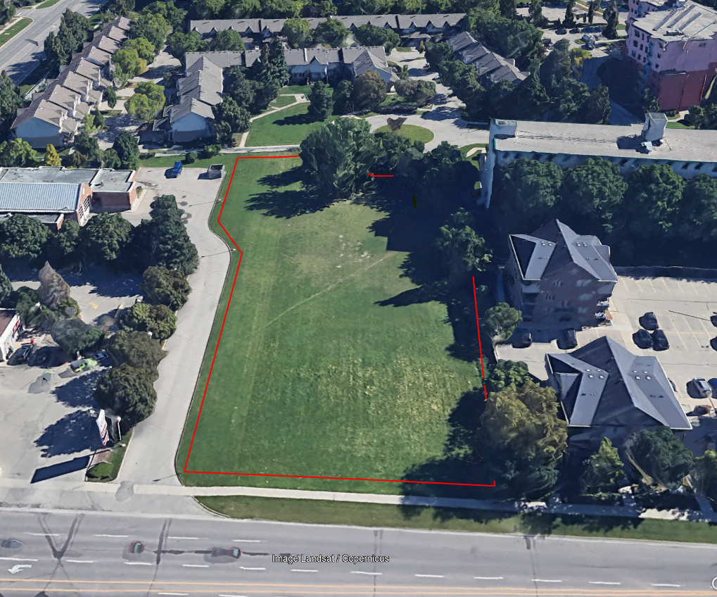 A birds eye view of a green field between residential , commercial, and service developments. and abutting a road. The field has been donated for housing construction.