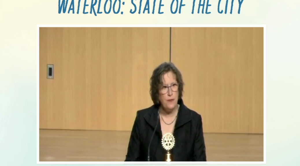 A screenshot of the video from Mayor McCabe's State of the City. The Text Waterloo State Of the City is above Mayor McCabe standing with a mic infront of her.
