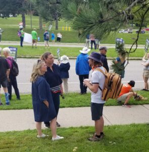 Ontario NDP leader Marit Stiles standing with local NDP MPP Catherine Fife. They are having a friendly chat with a rally participant. Others at the demo are in the background.